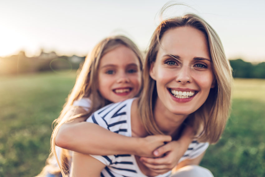 mother giving her daughter a piggyback - happy family